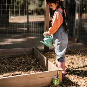 Culbuto-composteur petite fille utilisant un arrosoir dans un enclos.